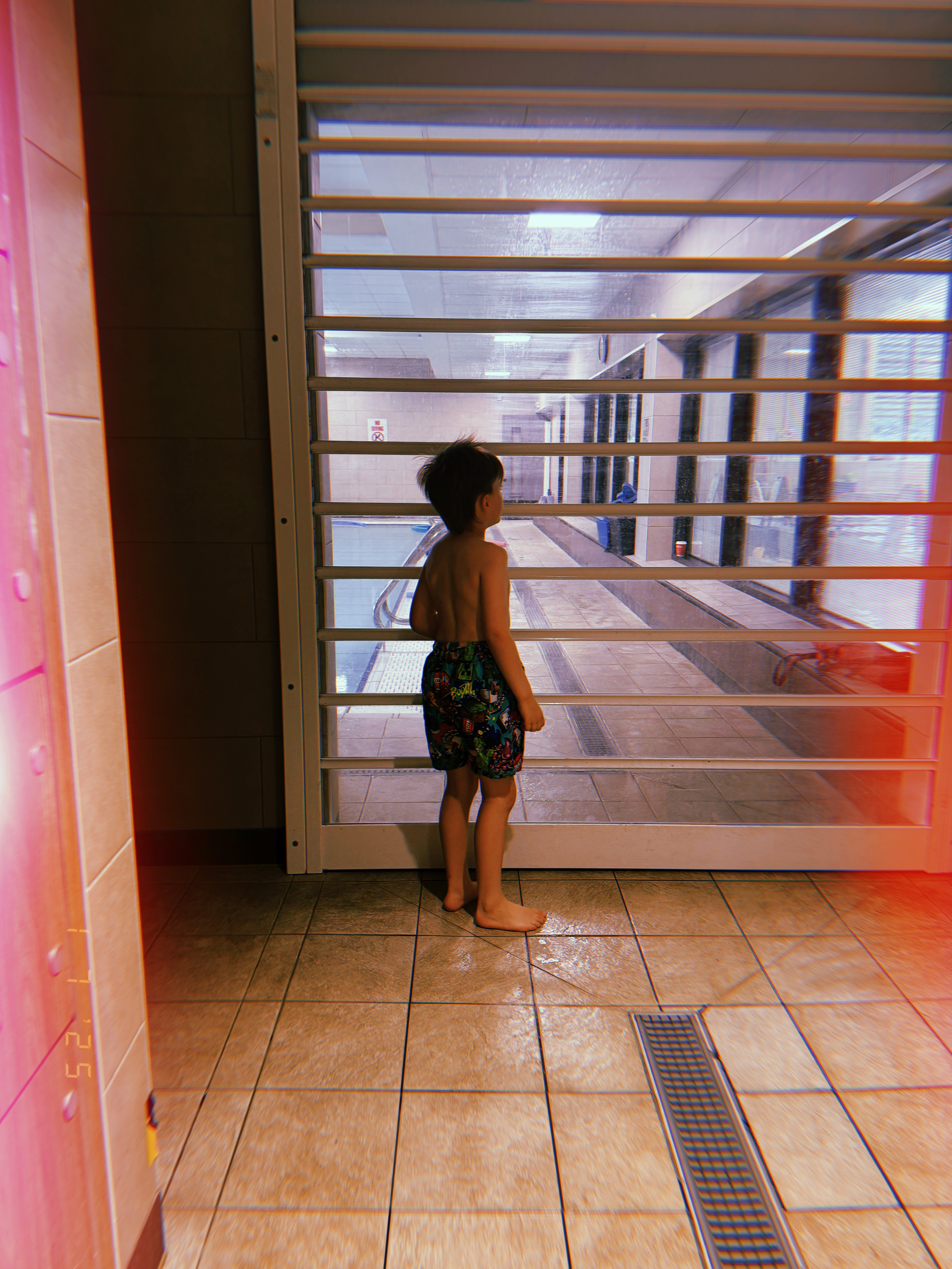 kid in swimming trunks facing swimming pool